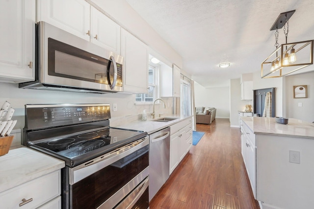 kitchen featuring wood finished floors, a sink, stainless steel appliances, white cabinetry, and decorative light fixtures