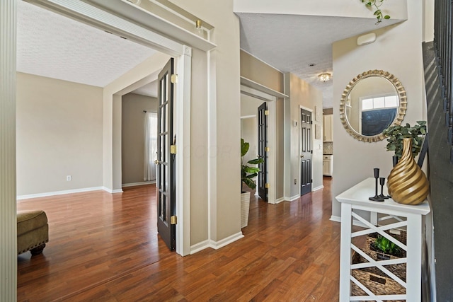 hall featuring plenty of natural light, wood finished floors, baseboards, and a textured ceiling