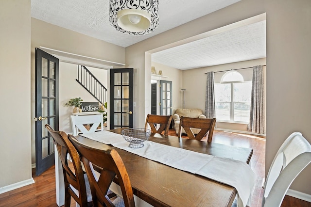 dining space featuring french doors, baseboards, a textured ceiling, and wood finished floors