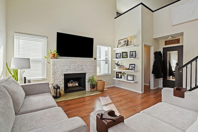 living room with baseboards, stairway, a stone fireplace, a towering ceiling, and wood finished floors