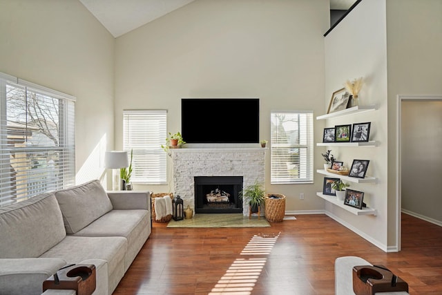 living area with baseboards, high vaulted ceiling, wood finished floors, and a fireplace