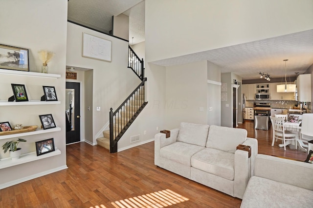 living area with visible vents, baseboards, stairway, a high ceiling, and dark wood-style flooring