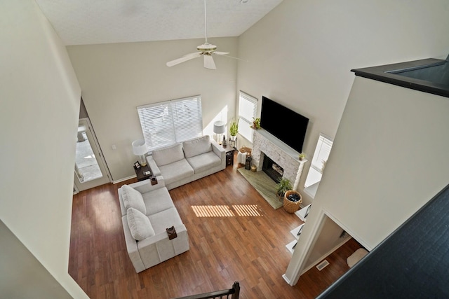 living area featuring high vaulted ceiling, a ceiling fan, wood finished floors, baseboards, and a brick fireplace