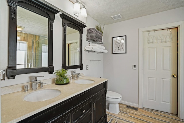 full bath featuring a sink, visible vents, toilet, and a textured ceiling