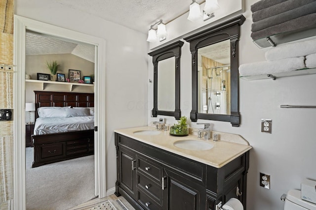 ensuite bathroom featuring a textured ceiling, double vanity, toilet, and a sink