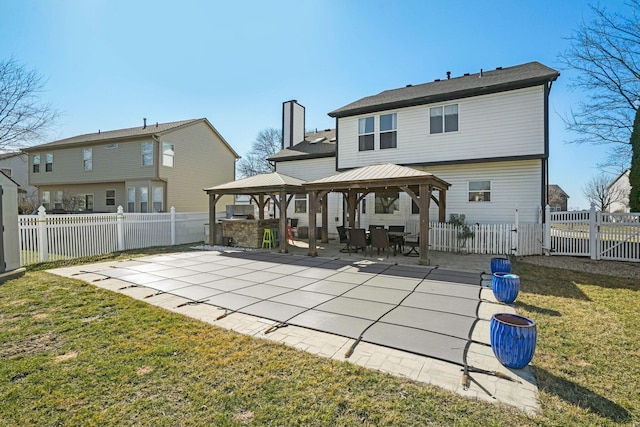 rear view of property featuring a fenced backyard, a chimney, a gazebo, a patio area, and a lawn