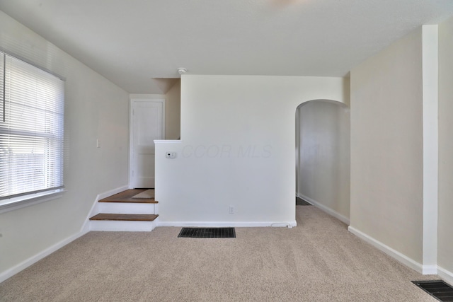 carpeted spare room with visible vents, baseboards, and arched walkways