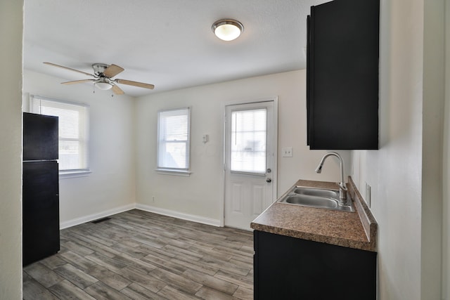 kitchen featuring wood finished floors, baseboards, visible vents, freestanding refrigerator, and a sink