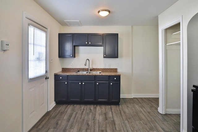 kitchen with a sink, baseboards, dark wood-type flooring, and dark countertops