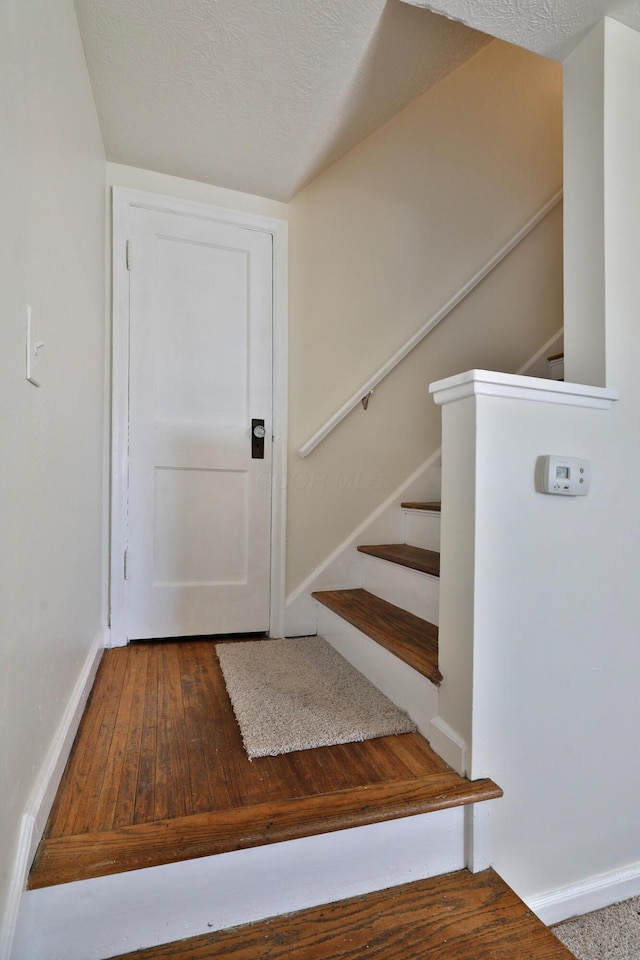 staircase featuring baseboards, a textured ceiling, and hardwood / wood-style floors