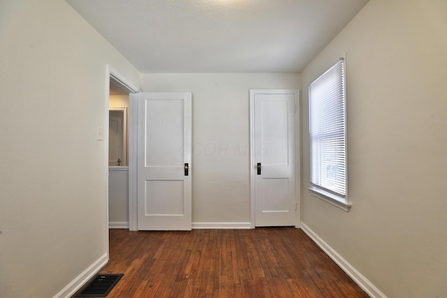 unfurnished bedroom with dark wood-style floors, visible vents, and baseboards