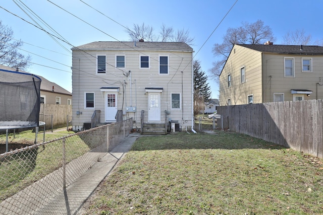 back of property with a fenced backyard, central air condition unit, a lawn, and a trampoline