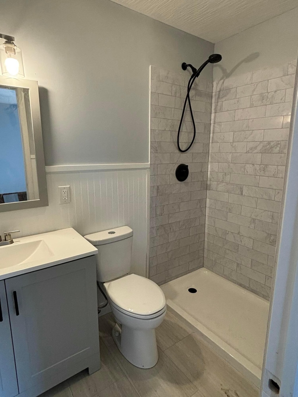 bathroom with vanity, toilet, a tile shower, and wainscoting