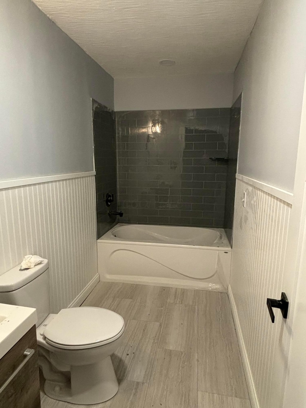 full bath featuring vanity, bathing tub / shower combination, toilet, and a wainscoted wall