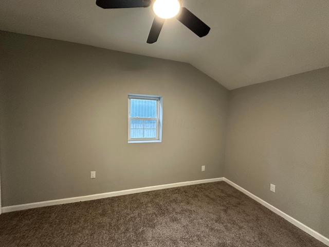 spare room with vaulted ceiling, baseboards, dark carpet, and ceiling fan