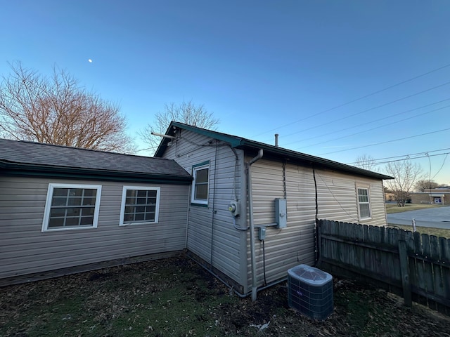 view of side of home featuring central air condition unit, a shingled roof, and fence