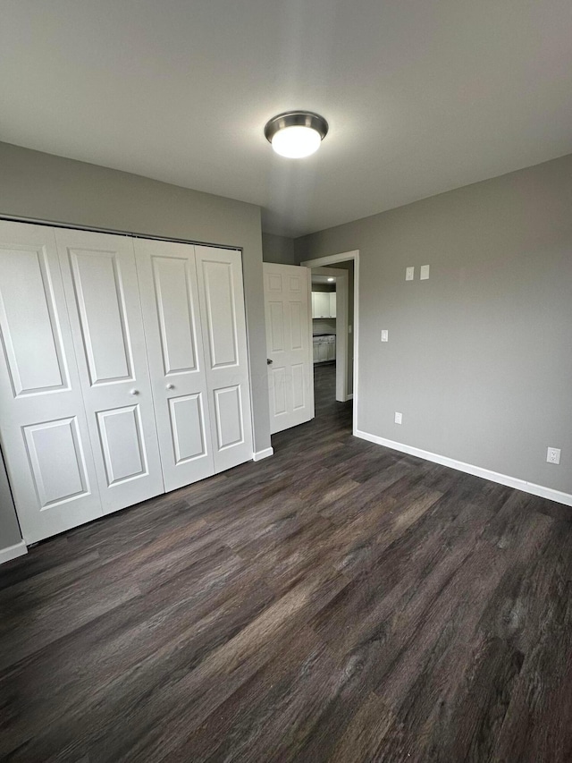 unfurnished bedroom featuring baseboards, a closet, and dark wood-style flooring