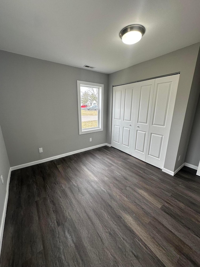 unfurnished bedroom featuring a closet, visible vents, dark wood-type flooring, and baseboards