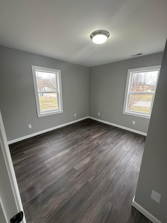 unfurnished room featuring visible vents, baseboards, dark wood-type flooring, and a healthy amount of sunlight