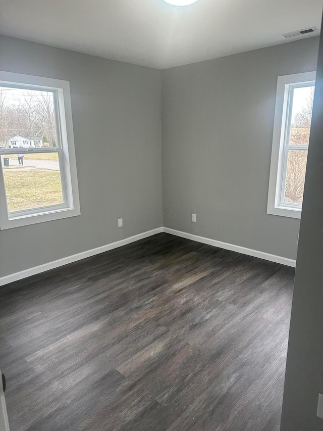 unfurnished room featuring dark wood finished floors, visible vents, and baseboards