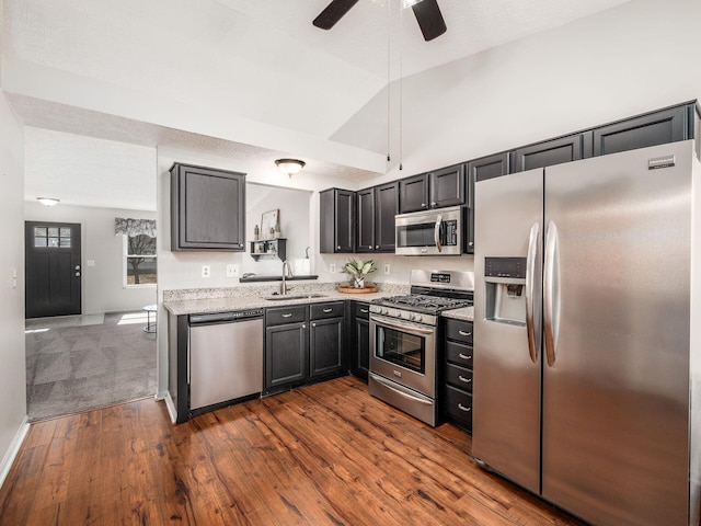 kitchen with light stone counters, dark wood-style floors, a sink, vaulted ceiling, and appliances with stainless steel finishes