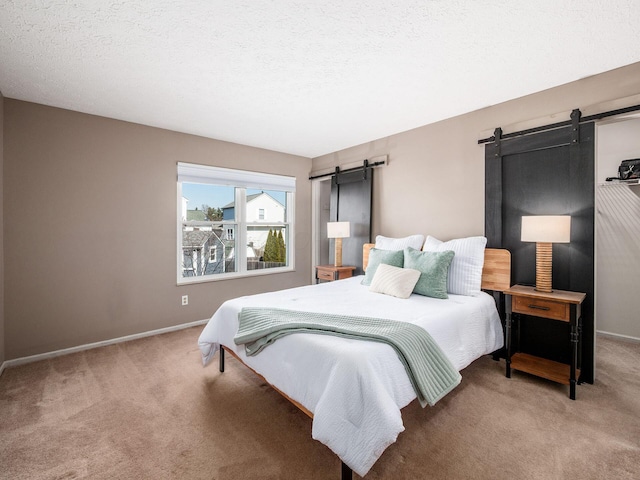 bedroom featuring a barn door, carpet, baseboards, and a textured ceiling