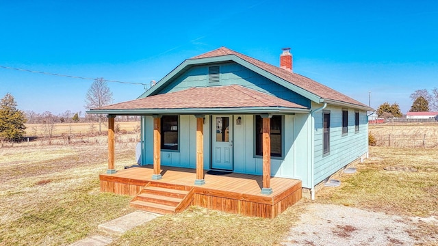 bungalow-style house with a chimney, covered porch, and a shingled roof