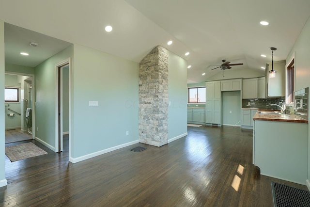 unfurnished living room with baseboards, visible vents, dark wood finished floors, a sink, and vaulted ceiling