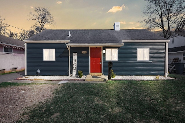 view of front facade featuring a front yard, roof with shingles, and a chimney