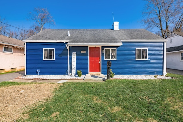 view of front facade featuring a front yard, a chimney, and a shingled roof