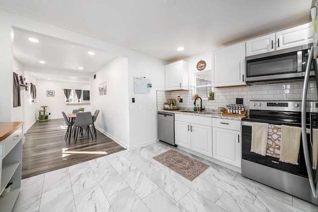 kitchen featuring marble finish floor, a sink, backsplash, appliances with stainless steel finishes, and white cabinets