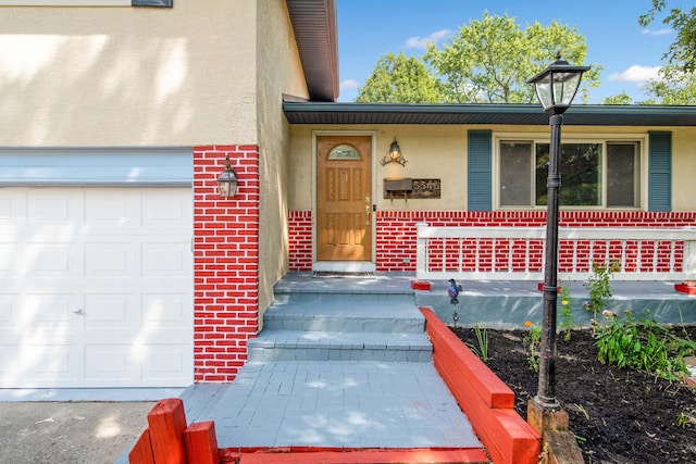 property entrance with stucco siding, brick siding, covered porch, and an attached garage