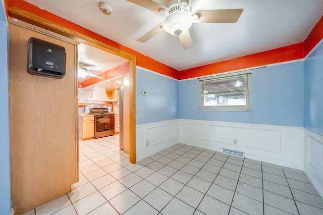 empty room featuring light tile patterned flooring, visible vents, ceiling fan, and a wainscoted wall