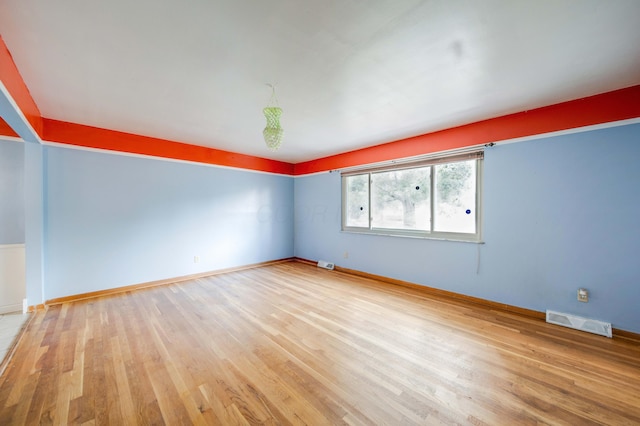 unfurnished room featuring visible vents, baseboards, and wood finished floors