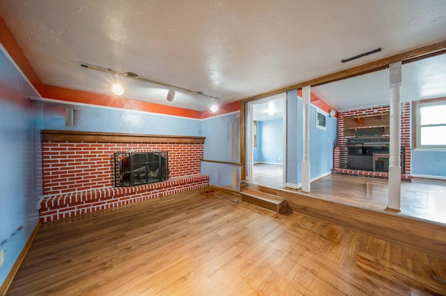 unfurnished living room featuring wood finished floors, baseboards, visible vents, a fireplace, and a textured ceiling