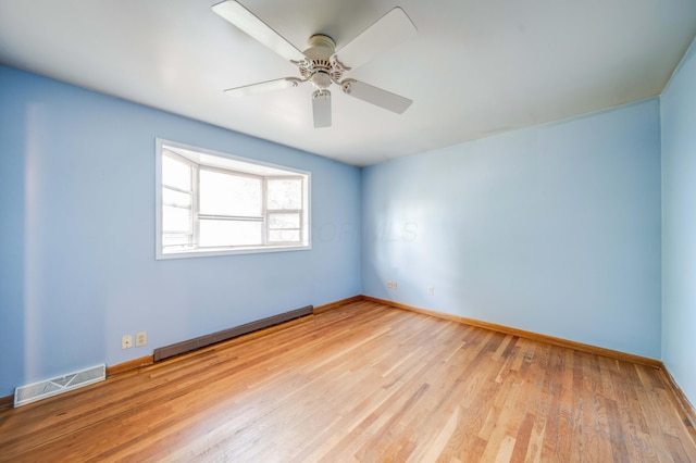 empty room featuring wood finished floors, baseboards, visible vents, a baseboard radiator, and ceiling fan