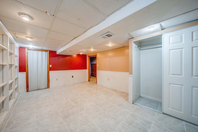 finished basement with visible vents, a paneled ceiling, and wainscoting