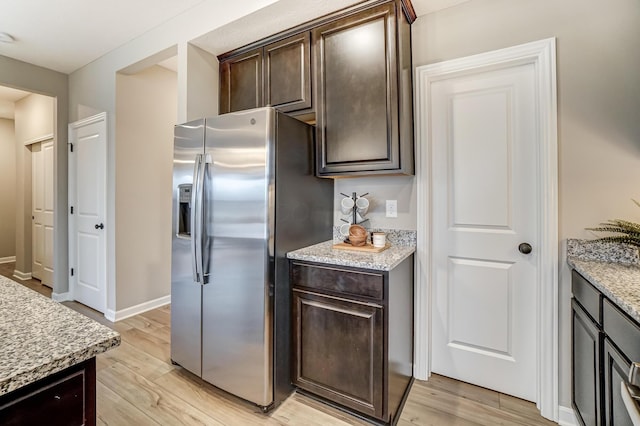 kitchen with dark brown cabinets, light stone countertops, stainless steel refrigerator with ice dispenser, and light wood finished floors