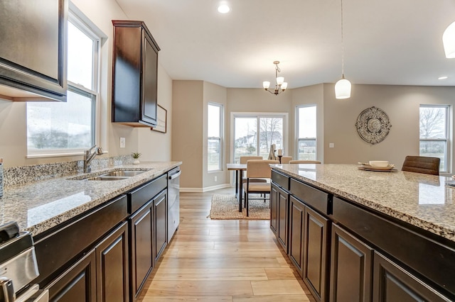 kitchen featuring pendant lighting, light stone counters, appliances with stainless steel finishes, light wood-style floors, and a sink