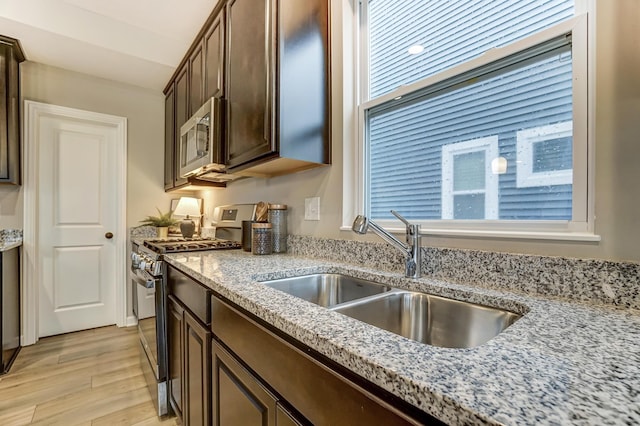 kitchen featuring light stone counters, a sink, dark brown cabinetry, light wood-style floors, and appliances with stainless steel finishes