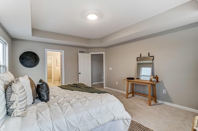 bedroom with visible vents, light carpet, a tray ceiling, ensuite bath, and baseboards