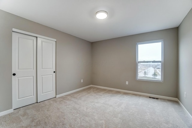 unfurnished bedroom with visible vents, light colored carpet, a closet, and baseboards