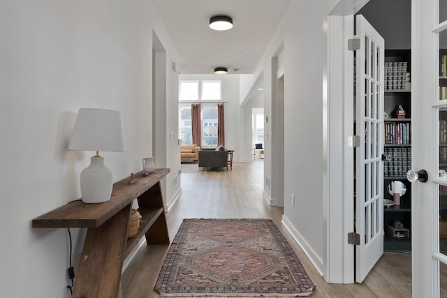 corridor featuring light wood-style floors, baseboards, and french doors