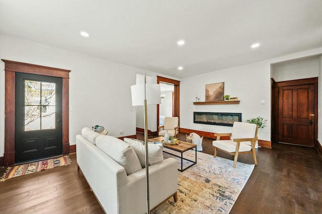 living room featuring a glass covered fireplace, recessed lighting, baseboards, and wood finished floors