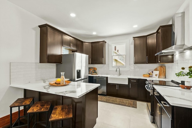 kitchen featuring a sink, appliances with stainless steel finishes, a peninsula, wall chimney range hood, and dark brown cabinets