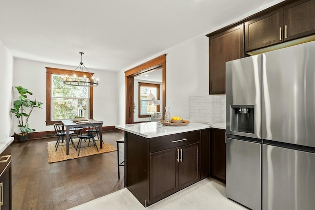 kitchen with tasteful backsplash, a peninsula, stainless steel fridge with ice dispenser, light countertops, and dark brown cabinets