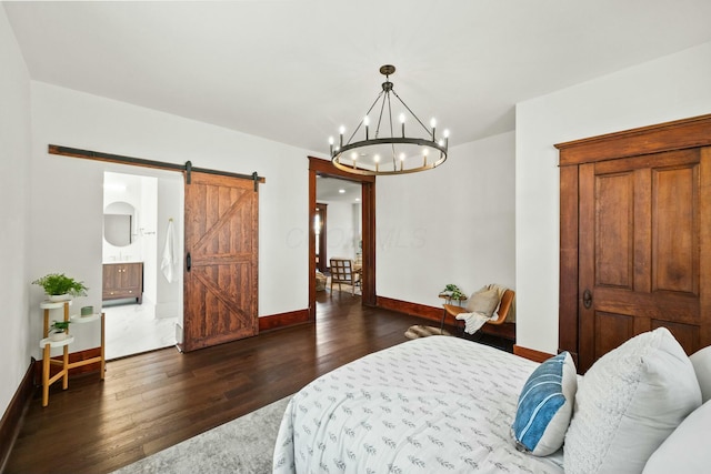 bedroom featuring ensuite bathroom, dark wood-style floors, a barn door, an inviting chandelier, and baseboards