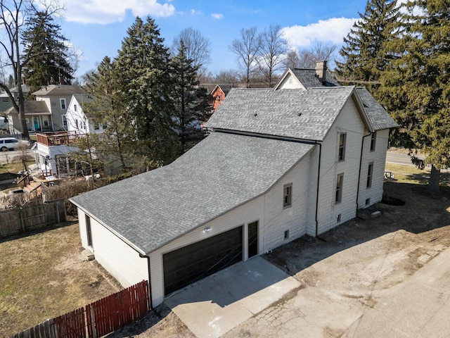 view of side of property with driveway, a shingled roof, a garage, and fence