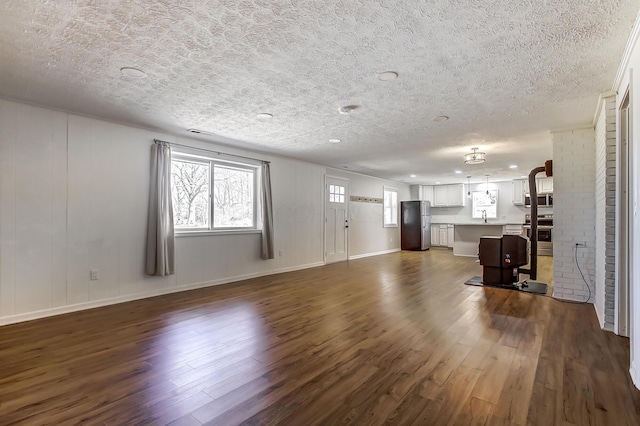 unfurnished living room with a textured ceiling, dark wood-type flooring, baseboards, and a sink