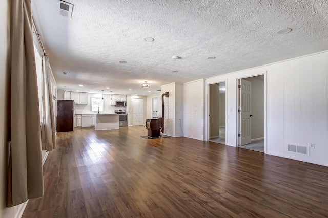 unfurnished living room featuring a sink, dark wood-type flooring, visible vents, and a textured ceiling